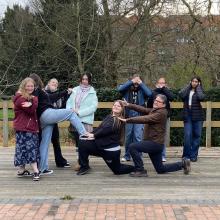 A group of people on the outdoor theatre stage in the Robinson gardens posing for a photo in a 'dramatic' style.